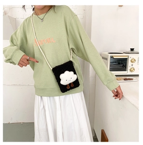 Close-up of black fleece crossbody bag with a cute smiling cloud plush on green hoodie