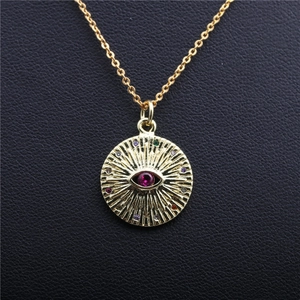 Gold necklace with pave zircon evil eye pendant and red center gem on black leather background