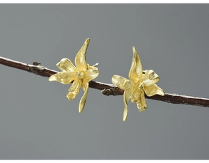 Macro detail of golden flower stud earrings with brushed metal texture on wooden branch