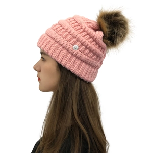Close-up of pink knitted beanie featuring a rose metal logo and fluffy fur pom-pom