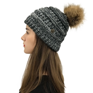 Detailed close-up of a knit beanie with a brown faux fur pom pom and a floral metal buckle