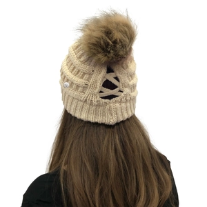 Detail of cream knit beanie with ponytail hole design and brown faux fur pom pom