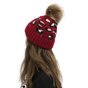 Close-up of red knit beanie featuring leopard pattern and a fluffy brown faux fur pom