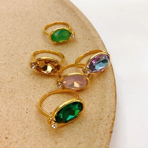Detailed top view of five gold plated rings with colorful oval gemstones on a beige plate