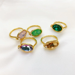 Set of five gold rings with oval colored gemstones on soft white fabric background