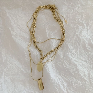 Detail of layered gold necklaces with oval and rectangular pendants on textured paper