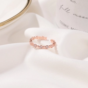 Close-up of rose gold star-shaped ring with zircon stones on white silk fabric