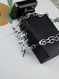 Macro shot of silver punk thorn chain with abstract graffiti pendant on a black prop