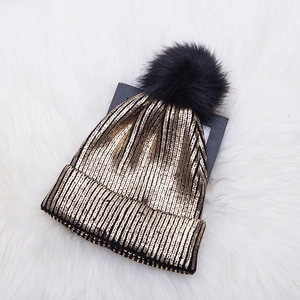 Golden and black knit beanie with pompom on plush white background for winter warmth