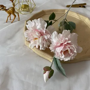 Close-up of pink artificial peony with blooming heads and soft flocked leaves on a tray