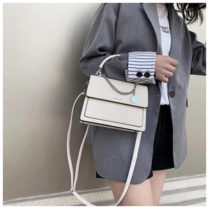 Detail of cream flap crossbody bag featuring silver chain decor and top handle strap