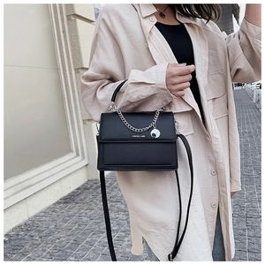 Outdoor street shot of black textured leather handbag with silver chain and logo detail