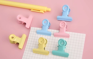 Flat lay of colorful macaron pastel binder clips on grid paper with a yellow pen
