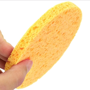 Hand holding a yellow round wood pulp sponge for facial cleansing and exfoliating