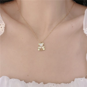 Detail of a golden bear necklace with white inlay and a Love engraved heart on a woman