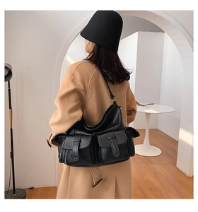 Detail view of a black multi-pocket PU leather tote bag worn with a beige coat