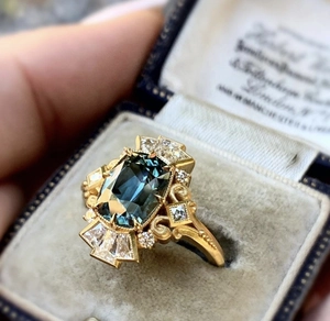 Close-up of gold ring with emerald-cut blue gemstone in a blue velvet vintage jewelry box