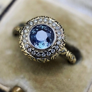 Vintage gold ring with blue round gemstone and floral carving in a beige jewelry box