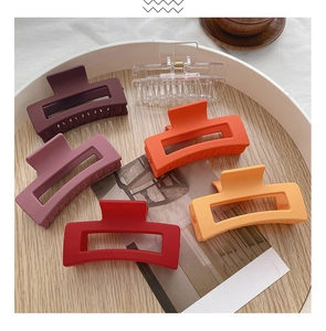 Close-up shot of multiple matte and clear acrylic hair claw clips arranged on a wooden tray.