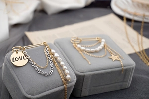 Detailed view of golden safety pins with fresh water pearls and tassel chains on velvet