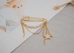 Close-up of gold safety pin brooch with freshwater pearls and star tassel charm