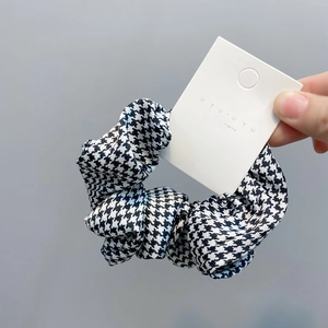 Macro view of elastic houndstooth scrunchie with soft pleated fabric and white tag