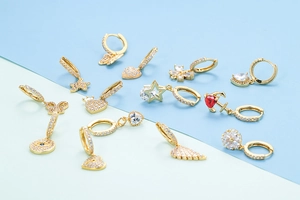 Flat lay of thirteen gold earrings with zircon charms on a blue and mint background