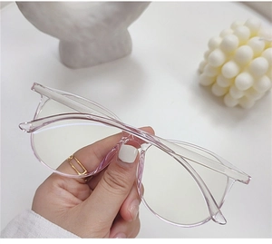 Detail of transparent pink-purple oversized glasses frame held by hand in soft light