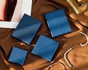 Detail of navy blue textured jewelry gift boxes on elegant brown silk with accessories