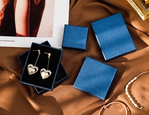 Detail of dark blue jewelry gift boxes with gold heart pearl earrings on brown velvet