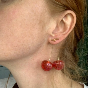 Close-up of cute red resin cherry earrings with gold stems worn by a model in soft light