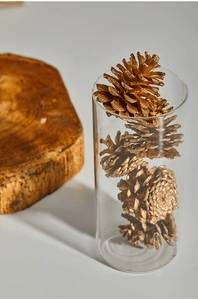 Golden natural pine cones in a cylindrical glass jar with a wooden base for Xmas decor