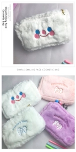 Close-up of plush makeup bag featuring colorful smiley embroidery and pearl zipper pull