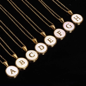Detail of gold round necklaces with A-H letters and white mother of pearl inlays