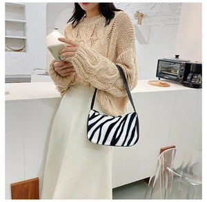 Close-up of zebra pattern faux fur shoulder bag held by a model in a cozy cafe setting