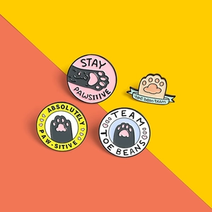 Close-up of four cute colorful cat paw enamel pins with motivational puns and shiny metal edges