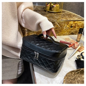 Close-up of black quilted PU leather makeup bag with handle and silver zippers on a desk