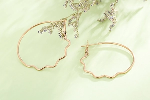 Detailed view of wavy rose gold hoop earrings with artistic dried flower and leaf shadows