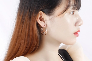 Close-up of rose gold knotted geometric hoop earrings worn by a model in bright light