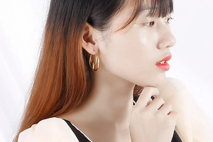 Close-up of a model wearing golden stainless steel geometric knotted hoop earrings