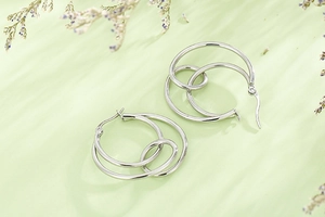 Detail of silver geometric knotted double hoop earrings on a light green background