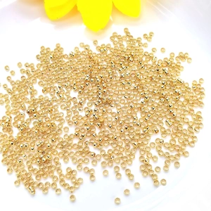 14K gold plated crimp beads for DIY jewelry making scattered on a white ceramic plate