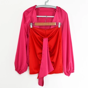 Dettaglio camicia in raso fucsia con scollo a V e completo minigonna a pieghe rossa