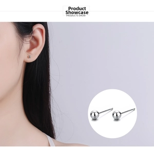 Close-up detail of silver ball stud earrings worn on the earlobe showing mirror finish