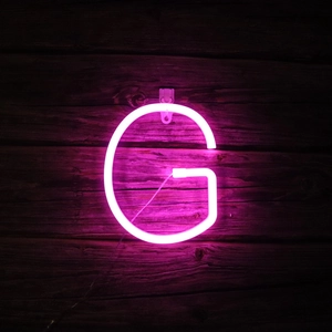 Pink LED neon letter G sign with wall hook on dark wood wall for room decoration
