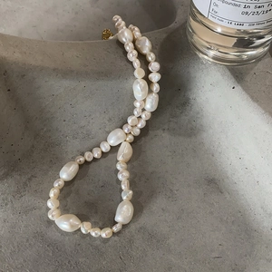 Macro view of baroque irregular pearl necklace with gold clasp on textured grey tray