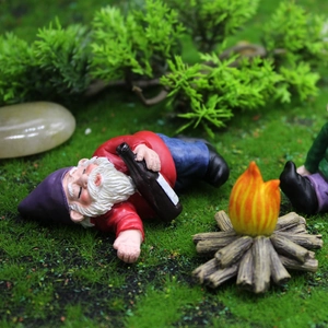 Nain de jardin humoristique en résine couché sur l'herbe avec petit feu de camp