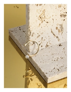 Detailed view of a gold pearl ear cuff on a travertine stone with a mirror reflection