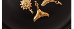 Detailed view of 18k gold plated sun face and whale tail pendants on dark plate