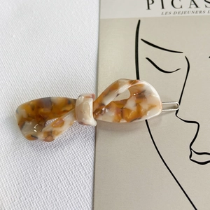 Detailed macro view of tortoiseshell pattern acetate bow hair clip on a minimalist card